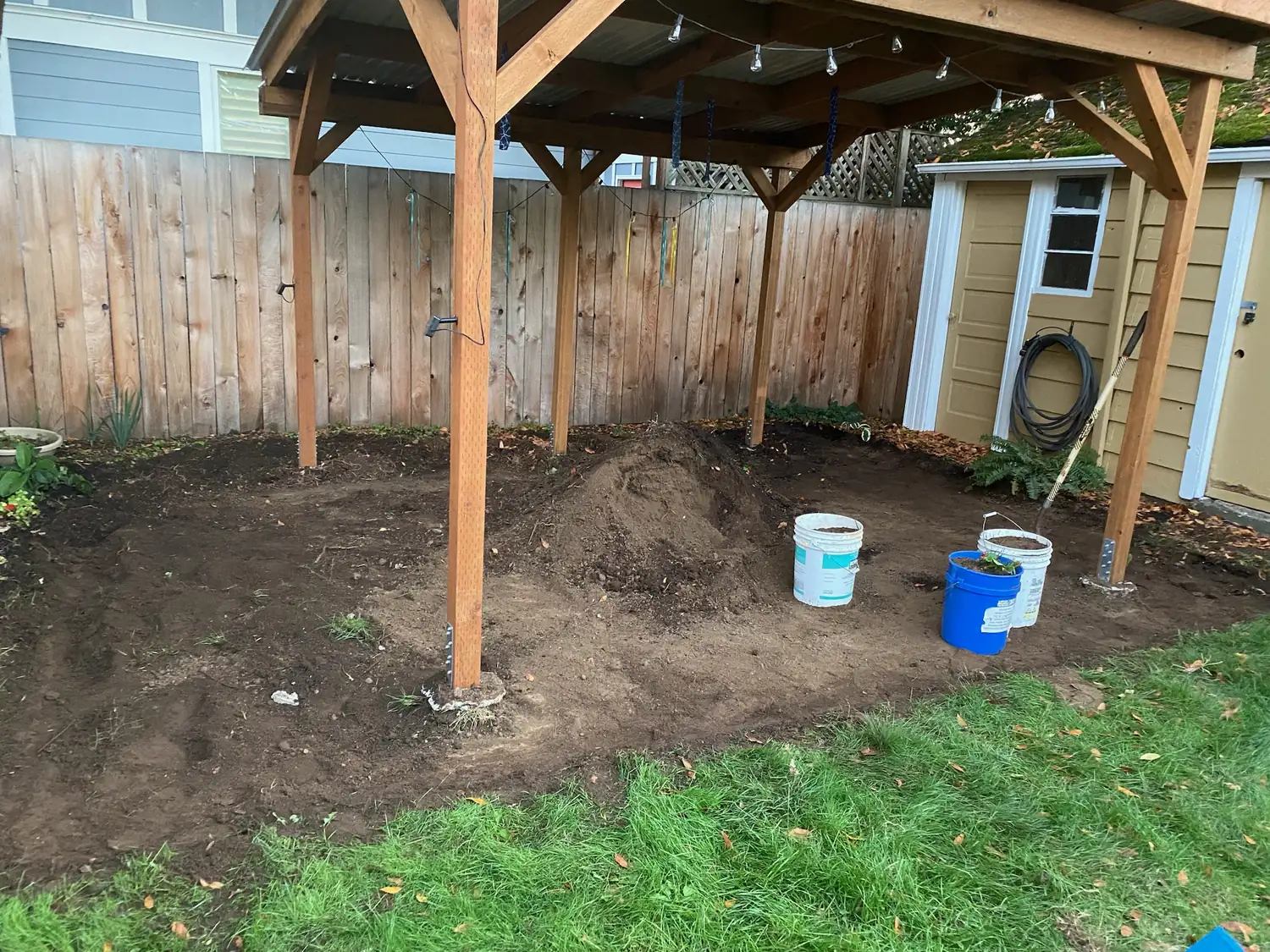 Bare soil and cedar posts standing where the new patio cover will go